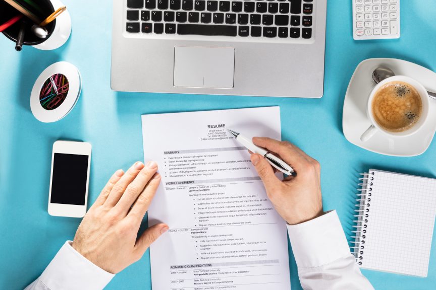 Elevated View Of A Businessman Reading Resume On Office Desk